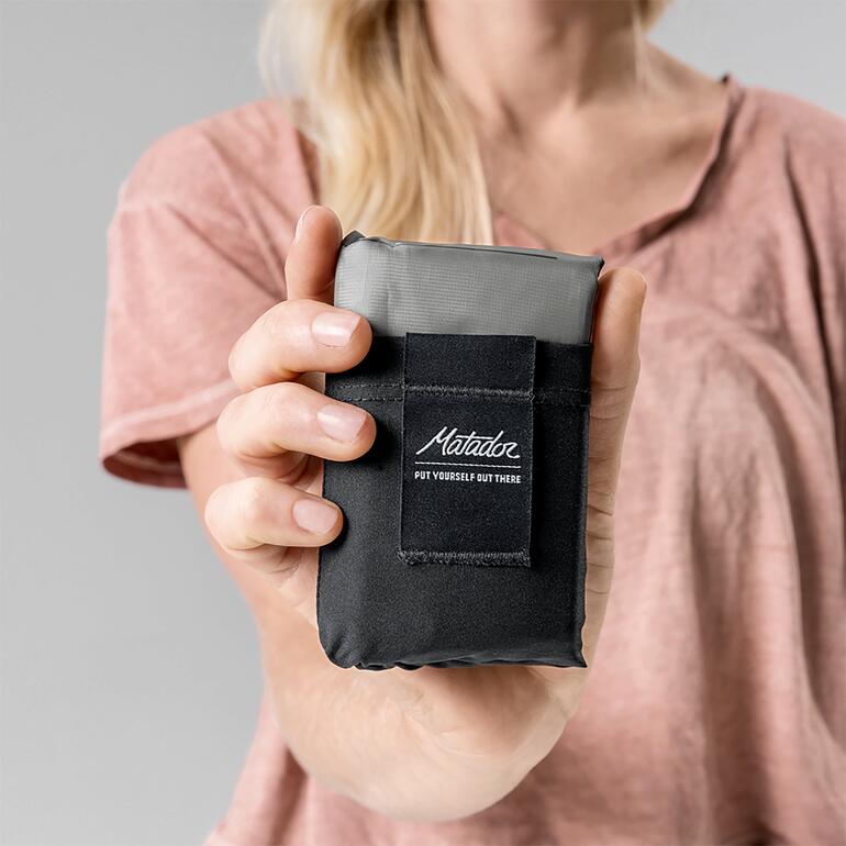 La couverture ne pèse que 108 grammes et mesure seulement 12 x 7,6 x 2,8 cm une fois repliée. Hand hält zusammengefaltete Ultraleicht-Taschen-Decke