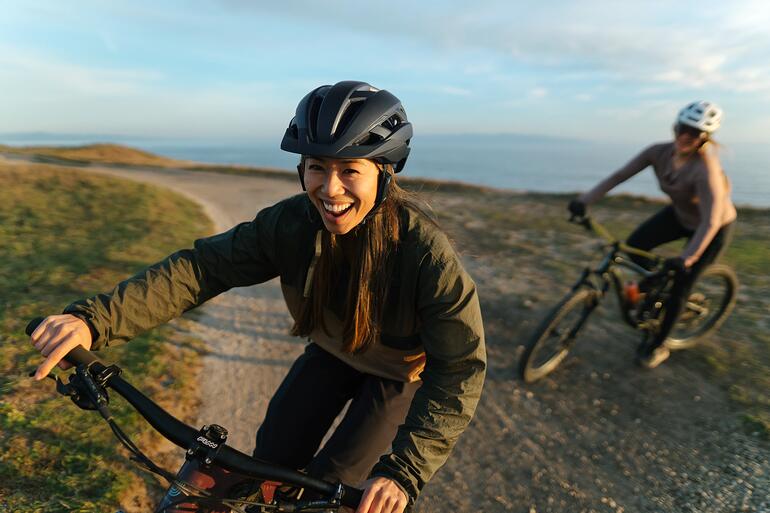 Beliebig grosse (Fahrrad-)Gruppen stehen miteinander in Sprechkontakt – kabellos und in glasklarer Audioqualität. Frau lacht auf dem Fahrrad, trägt einen Helm mit Intercom-System.