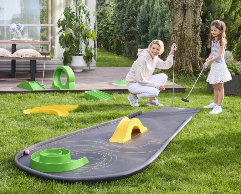 Frau mit Kind spielt Minigolf auf einem mitgenommenen Minigolfplatz.