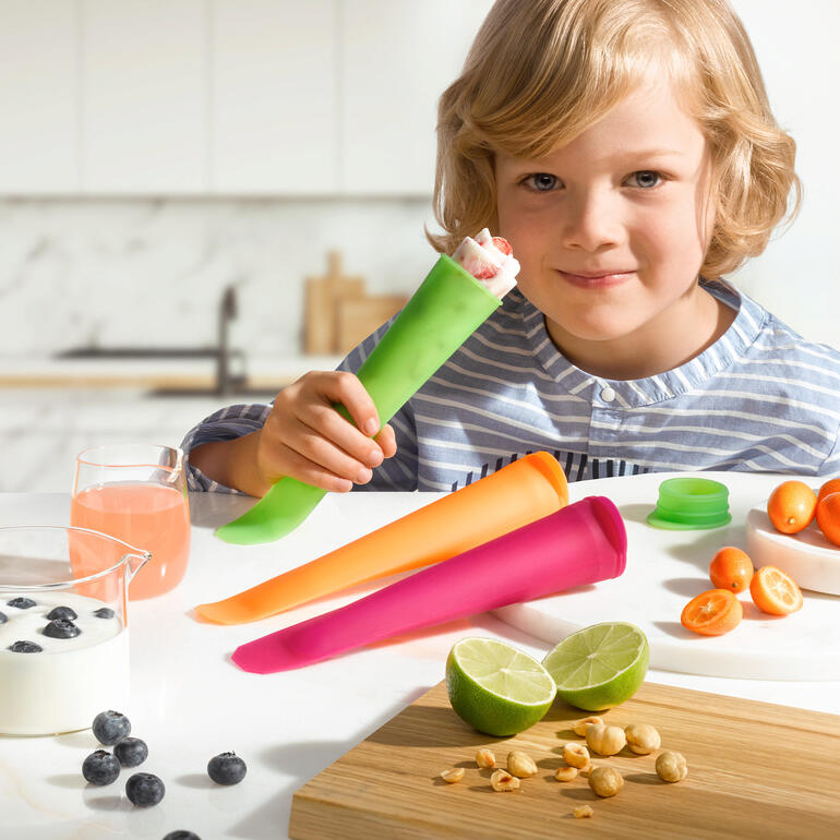 Süßes Kind mit Eis in Silikon-Eisform, umgeben von Früchten