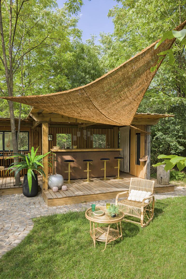 Sonnensegel aus Kokosfasern über einer Holzterrasse mit Barstühlen.