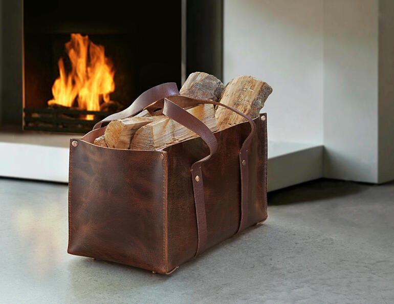 Die robuste Tasche fasst bis zu 8 Kilo Kaminholz, Zeitschriften, Gartenutensilien, ... Universal-Ledertasche aus Büffelleder mit Holzscheiten vor einem Kamin.