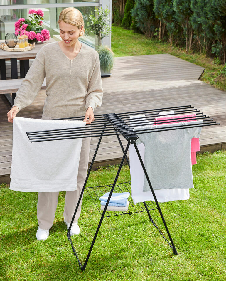Frau hängt Wäsche auf einem modernen Design-Wäscheständer im Garten auf