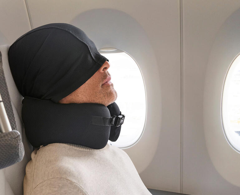 Mann mit Komfort-Reisekissen und Kapuze im Flugzeug