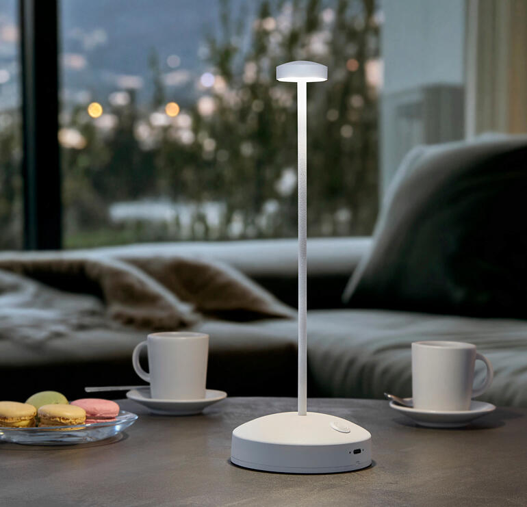 Weiss Design-Tischleuchte mit Akku, Farbe: Weiß, auf einem Tisch mit Getränken.