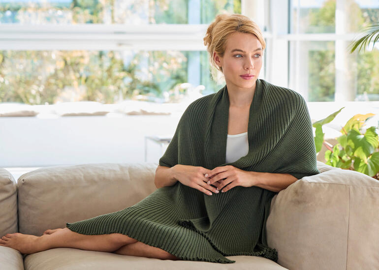 Frau in olivgrüner Plissee-Stola sitzt auf einem Sofa