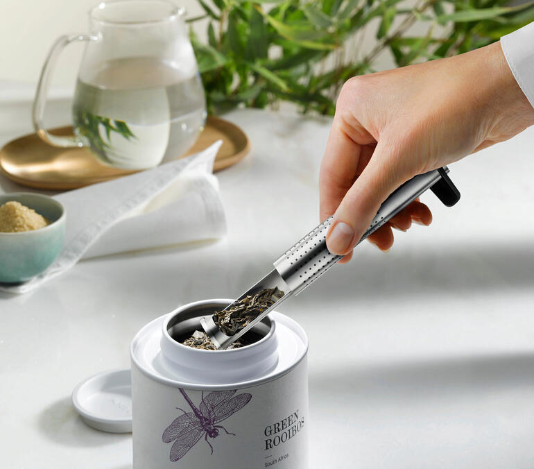 Einfach mit dem Langrohr-Teefilter entnehmen Sie Ihre gewünschte Menge Teeblätter direkt aus der Vorratsdose – kein zusätzlicher Löffel nötig. Hand greift nach dem Aroma-Langrohr-Teefilter