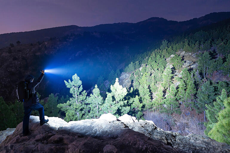 Les 6 LEDs à haut rendement offrent une lumière projetée dʼincroyables 5 000 lumens et la font rayonner jusquʼà 245 m de distance. Mann hält eine Taschenlampe in den Bergen bei Nacht.