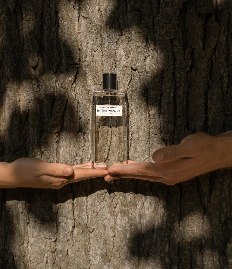 Flasche In the Woods Eau de Parfum in Händen, vor einem Baumstamm.