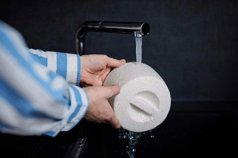 Einfach den Keramik-Butterkühler unter fliessendem Wasser tränken – der Kühleffekt entsteht durch Verdunsten des aufgesogenen Wassers. Person wäscht Keramik-Butterkühler unter fließendem Wasser.
