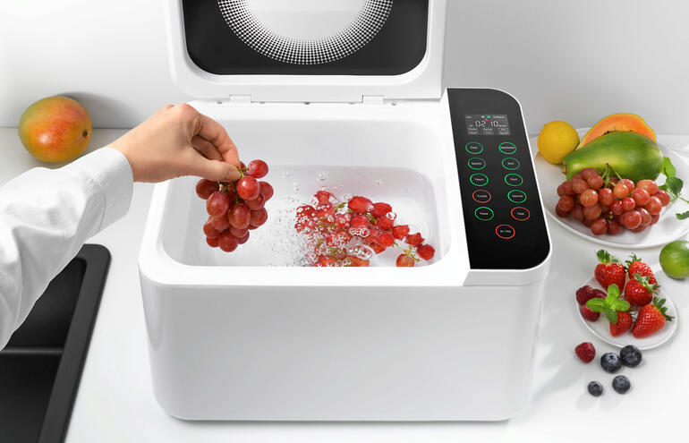 Hand greift nach Trauben in Food Washer, während Wasser sprudelt.
