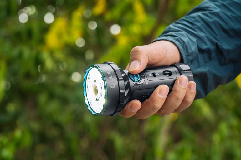 Intuitiv per Daumendruck umschaltbar. Mann hält eine Taschenlampe im Freien mit grünem Hintergrund.