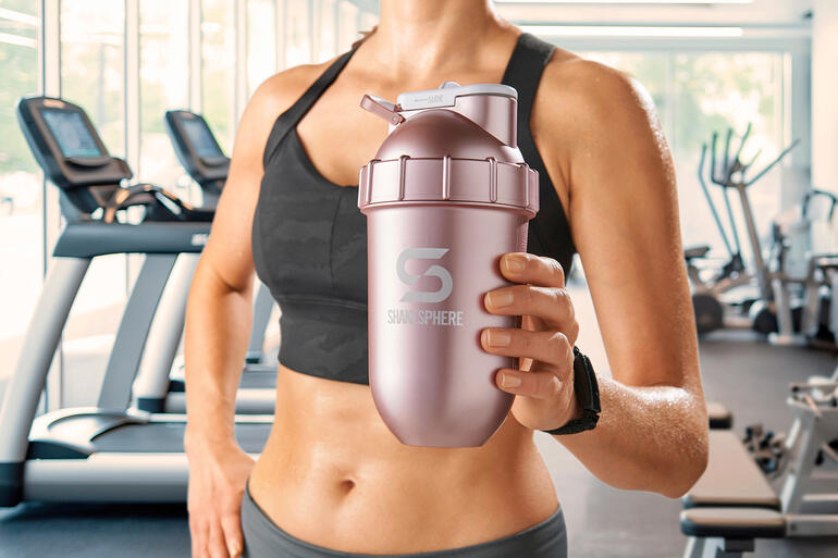 Frau hält einen rosa Shaker in einem Fitnessstudio.