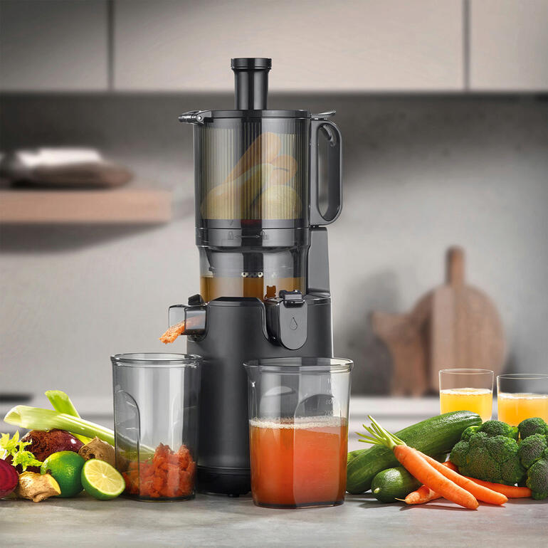 CASO Design Slow-Juicer mit frischem Gemüse und zwei Gläsern Saft auf einem Tisch