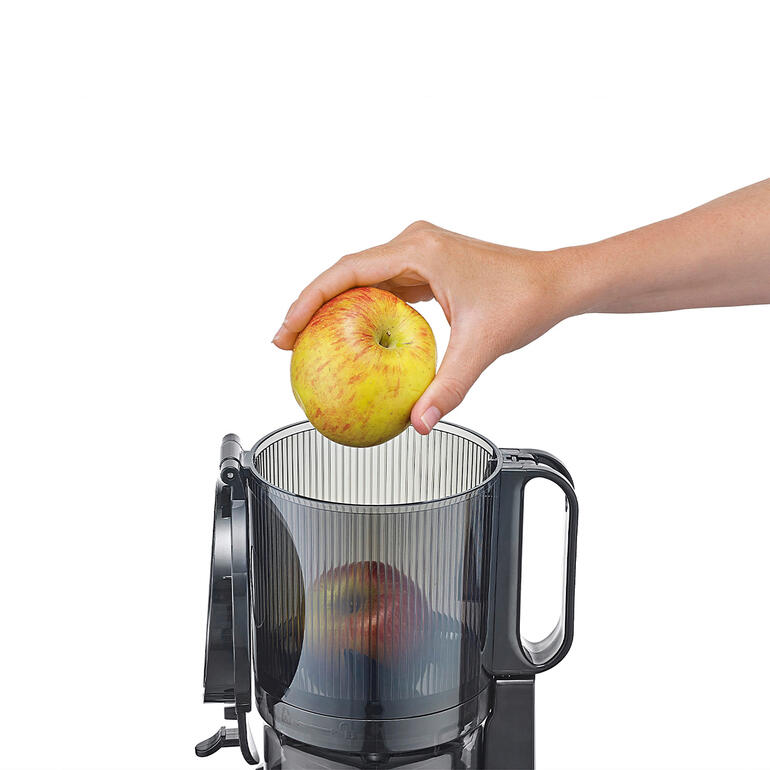 Mit 13 cm Ø grosser XXL-Einfüllöffnung – perfekt für ganze Früchte. Hand, die einen Apfel in das obere Fach des CASO Slow-Juicers legt