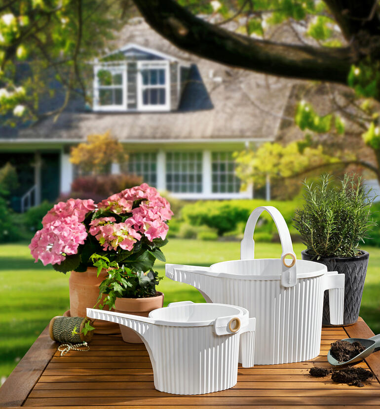 Zwei Gießkanne in Weiß und Blumen auf einem Tisch im Garten