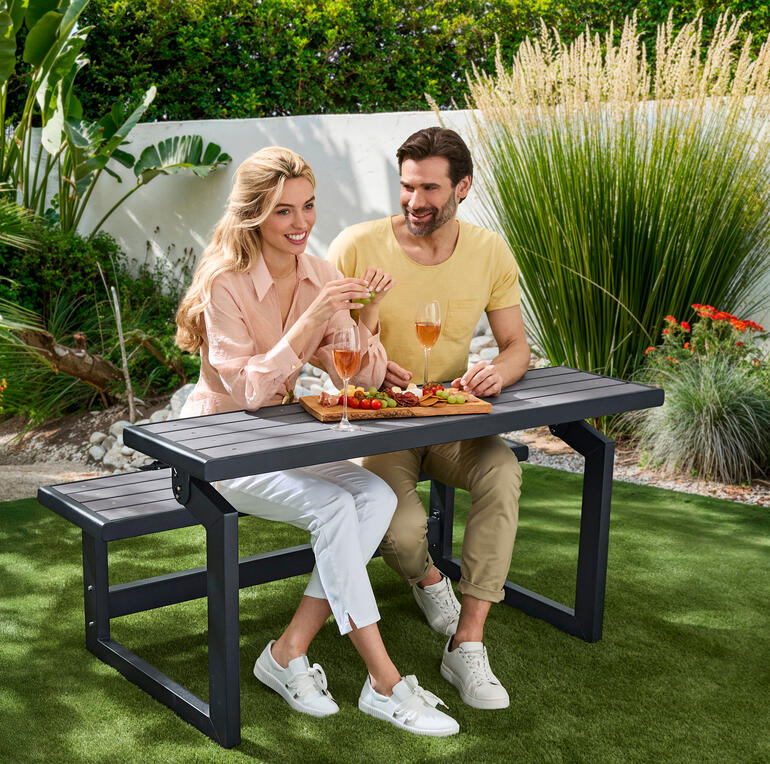 Paar sitzt an Vario-Picknicktisch im Garten und genießt Snacks und Getränke.
