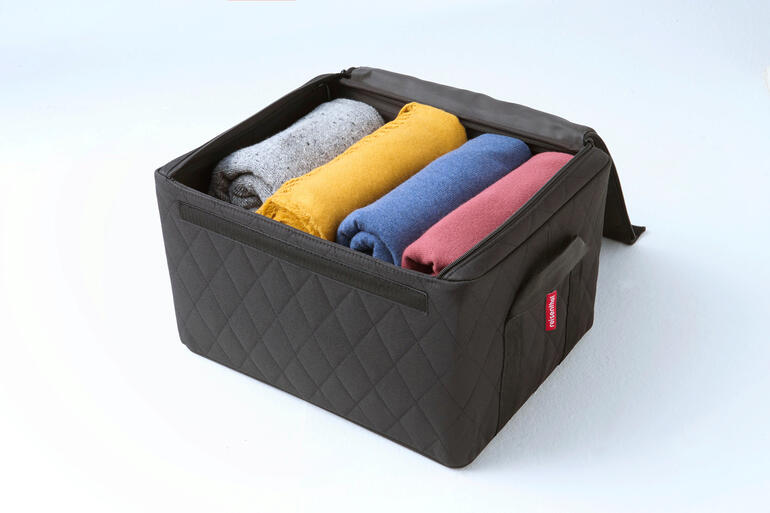 Stapelbox in Schwarz mit bunten gefalteten Handtüchern im Inneren.