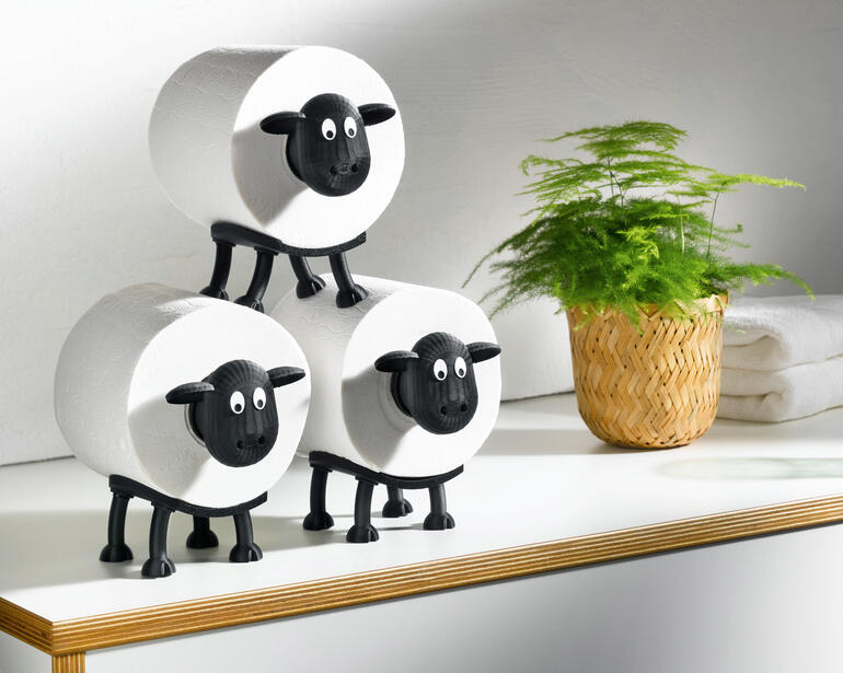 Drei Toilettenpapierhalter in Form von Schafen auf einem Tisch.