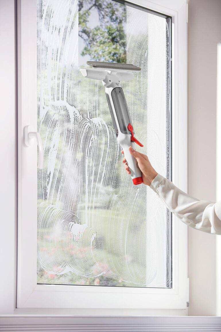 Person reinigt Fenster mit 3-in-1 Teleskop-Fensterwischer, Seifenlauge auf dem Glas.