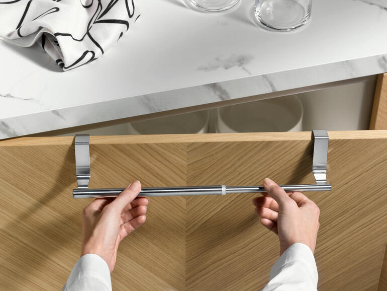 Ausziehbarer Handtuchhalter wird von Händen an einem Küchenschrank befestigt.