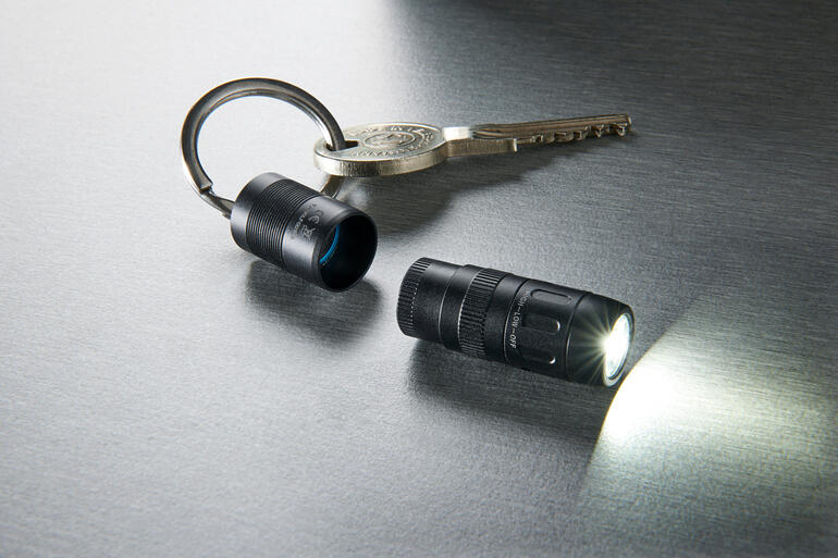 Magnet-Mini-Taschenlampe und Schlüssel auf schimmernder Oberfläche, Lampe leuchtet.