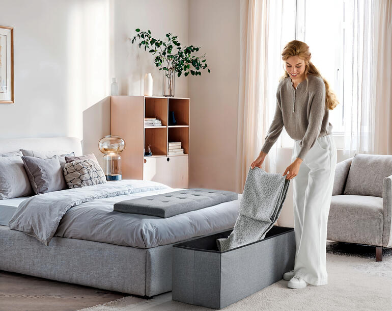 Faltbare Sitztruhe in Dunkelgrau, wird im Schlafzimmer genutzt.