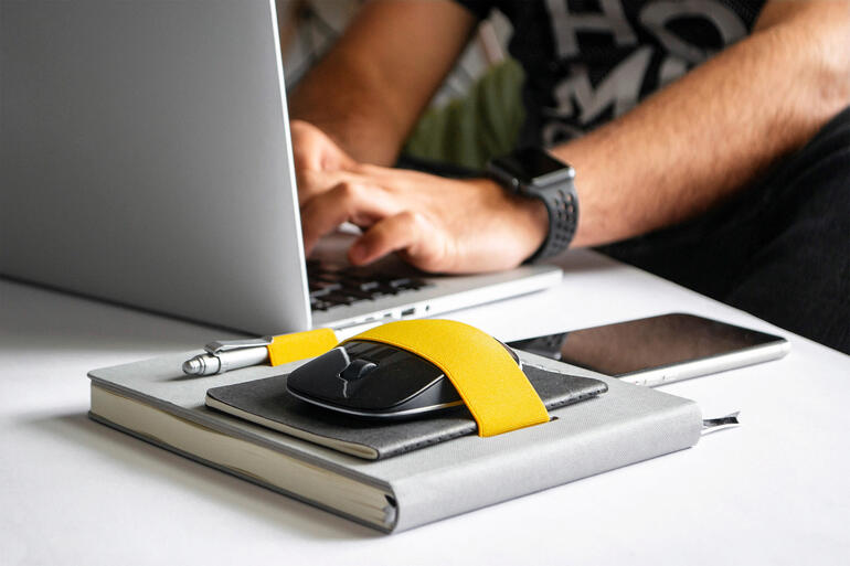 Person arbeitet mit einem Flex-Book, Laptop und Smartphone auf einem Tisch.