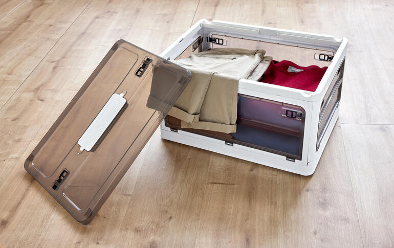 Offene Aufbewahrungsbox mit Kleidung auf Holzfußboden.
