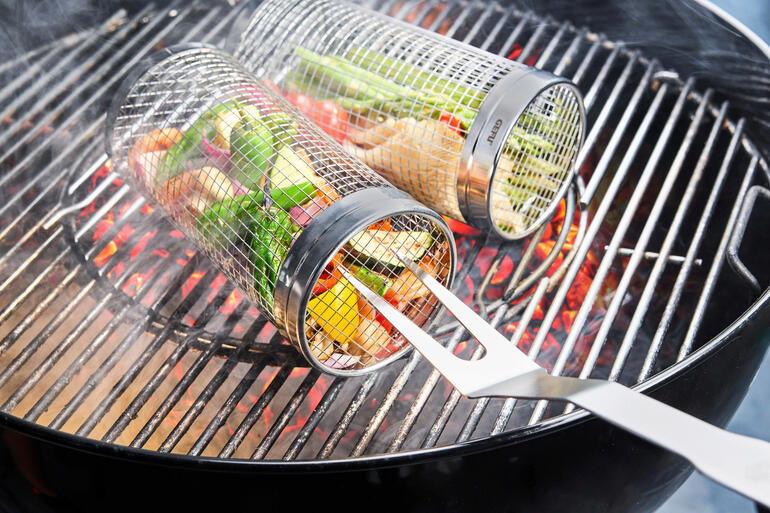 Grillkorb aus Metall mit Gemüse darin, auf dem Grill mit glühenden Kohlen.