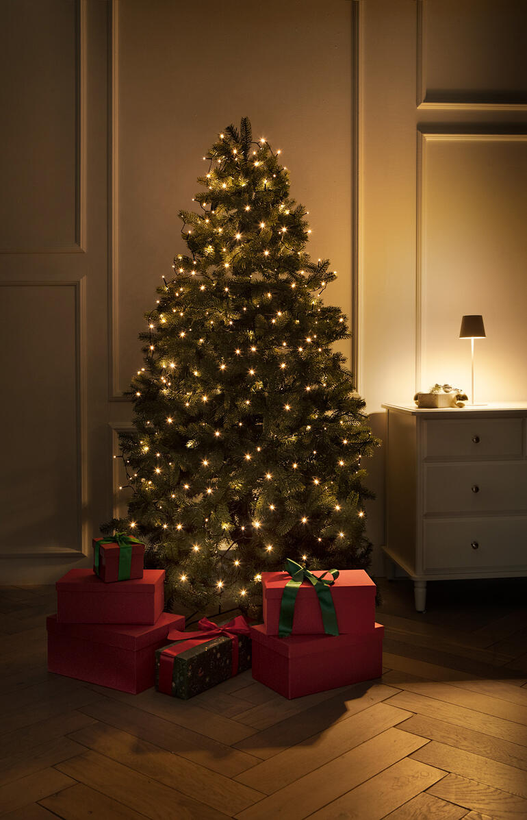 Beleuchteter Weihnachtsbaum mit Geschenken und warmem Licht in einem eleganten Raum.