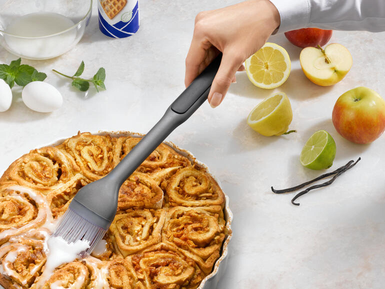 Hand mit einem Backpinsel, der einen warmen Zimtkuchen bestreicht.