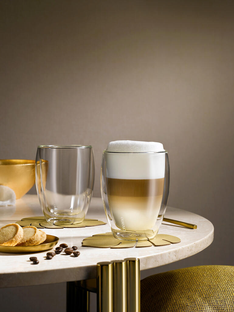 Zwei Premium-Thermogläser auf Tisch, eins mit schaumigem Getränk und eins leer.