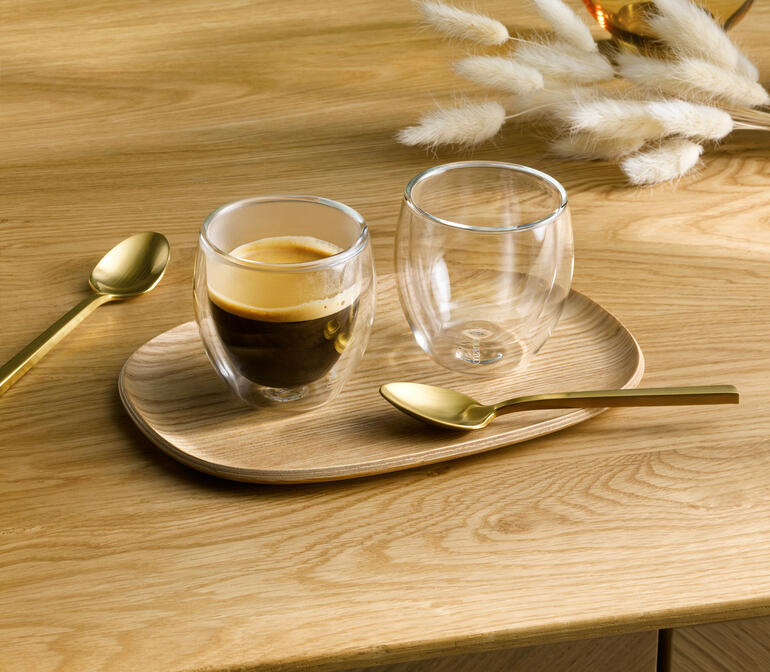 Zwei Premium-Thermogläser auf einem Holzbrett, eines enthält Espresso.