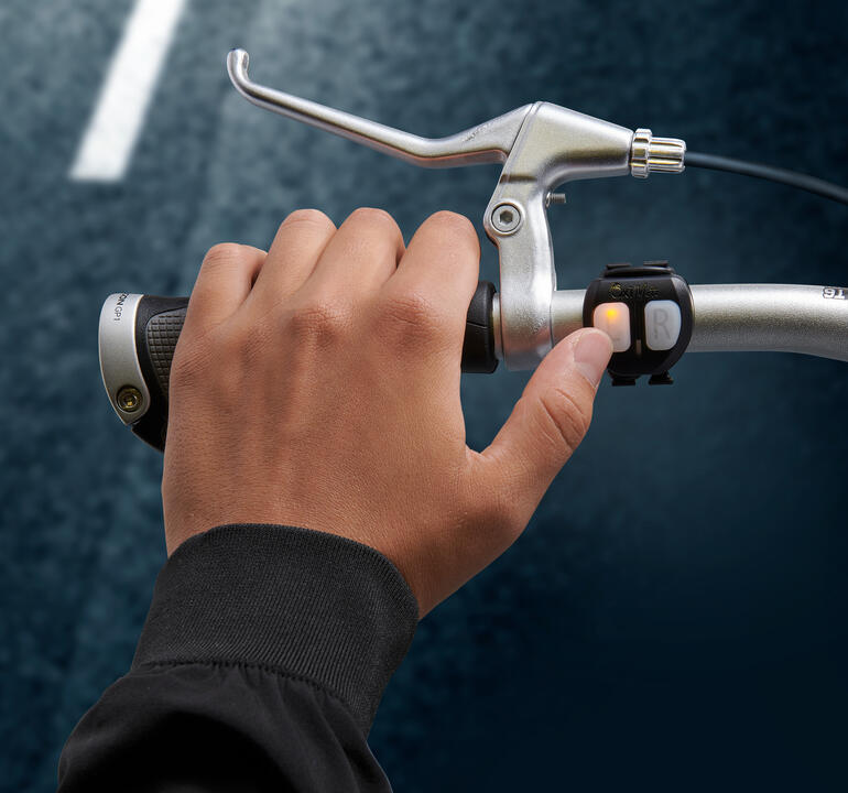 Hand drückt den Schalter für das Lichtsignal am Fahrradlenker