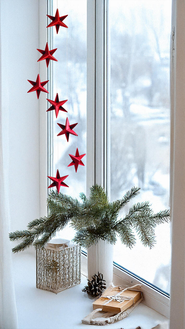 Rotes Mobiles Sternendekor über einer Fensterbank mit Schnee draußen.
