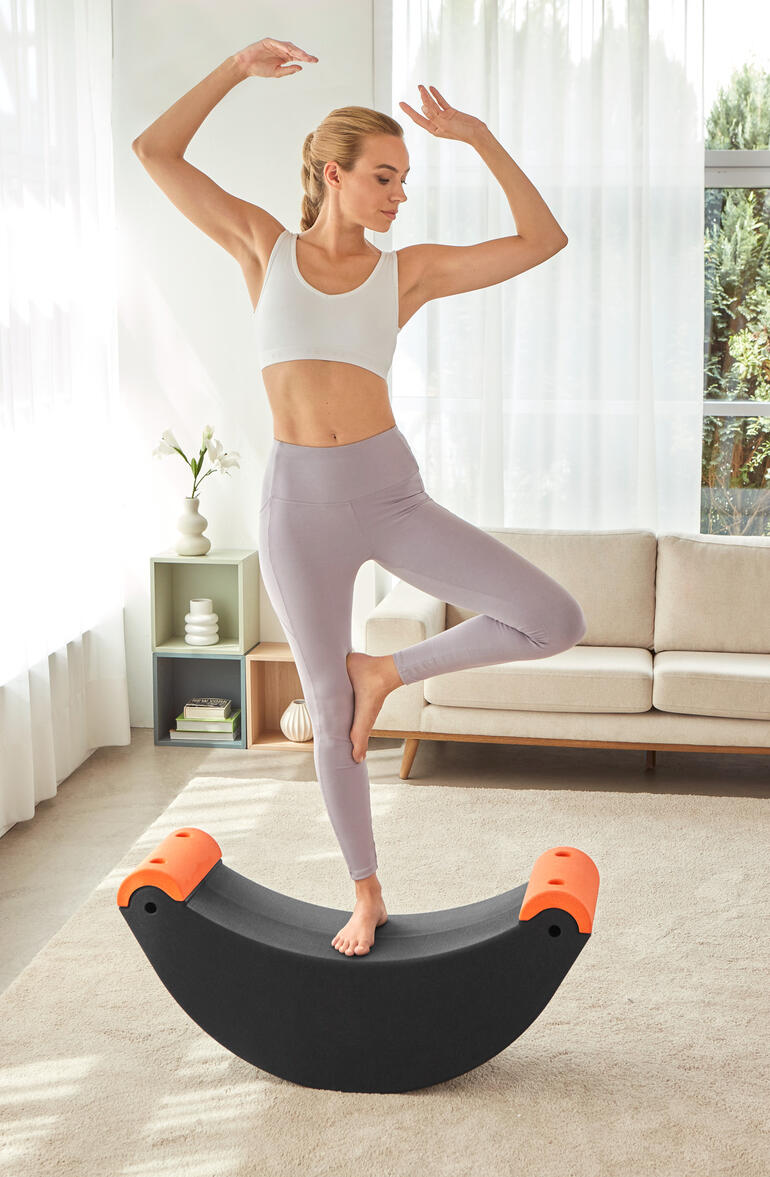Frau steht auf einem 3-in-1 Multifunktions-Trainer und balanciert auf einem Bein.
