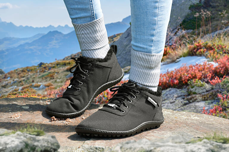 Für ein natürliches Laufgefühl – auch an kalten Tagen. Frau trägt schwarze Winter-Sneaker auf einer felsigen Unterlage in den Bergen.