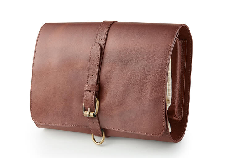Dank der Gürtelschnalle bleibt die zusammengerollte Kulturtasche sicher verschlossen. Büffelleder-Kulturtasche geschlossen mit Schnalle, auf weißem Hintergrund.