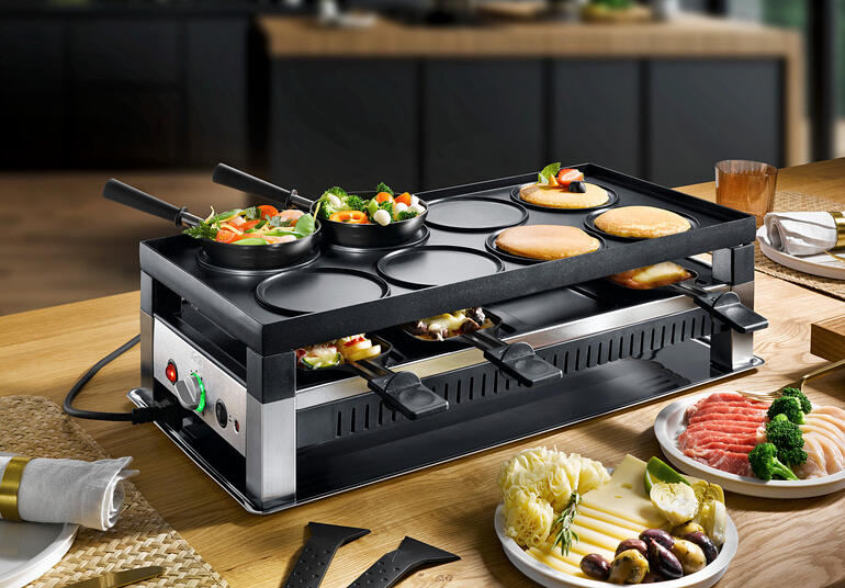 Solis Raclette- und Fun-Cooking 5-in-1 Gerät mit Gemüse und Fleisch auf dem Tisch.