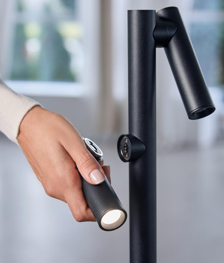 Hand greift nach der Taschenlampe der Stehleuchte für gezielte Beleuchtung.