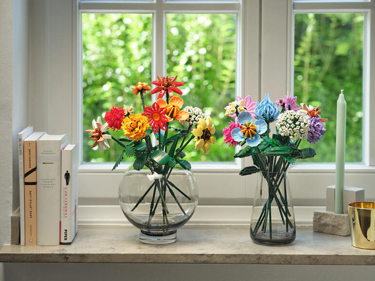 Einfach durch Zusammenstecken entstehen Bouquets von unvergänglicher Schönheit. Zwei Vasen mit bunten Blumen aus Klemmbausteinen auf einer Fensterbank.
