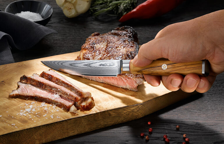 Die präzise geschliffene, glatte Klinge gleitet mühelos durchs Fleisch – ohne Saftverlust. Damast-Steakmesser in Verwendung, perfekt zum Schneiden eines Steaks.