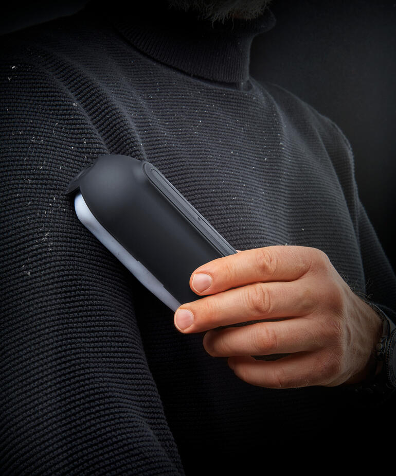 Ultraklebender Fusselroller in der Hand eines Mannes, mit Fusseln auf einem Pullover.