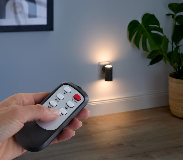 Fernbedienung für dimmbare Wandleuchte wird in der Hand gehalten.