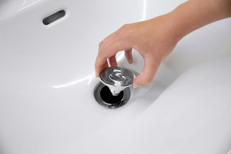 Hand greift nach dem Universal-Waschb. stöpsel mit Abflusssieb im Waschbecken.