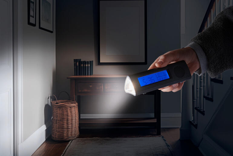 Hand hält einen Radiowecker mit LED-Taschenlampe im dunklen Raum.