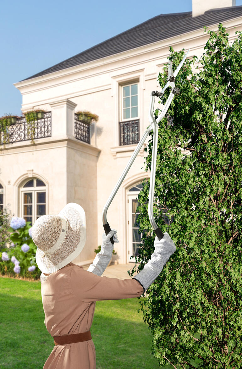 Frau schneidet mit einer Multiwinkel-Gartenschere hochgewachsene Pflanzen im Garten.