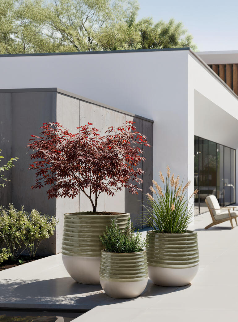 Drei Übertöpfe im Keramikdesign stehen auf einer Terrasse mit Pflanzen.