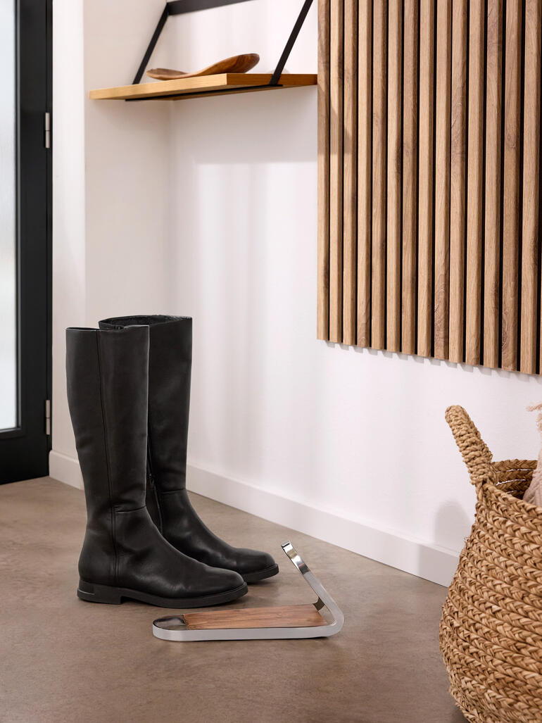 Schwarze Stiefel stehen neben einem modernen Stiefelknecht aus Holz und Metall.